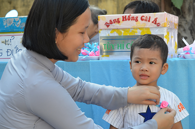 A Buddhist pinning a pink plastic rose on to a child’s dress