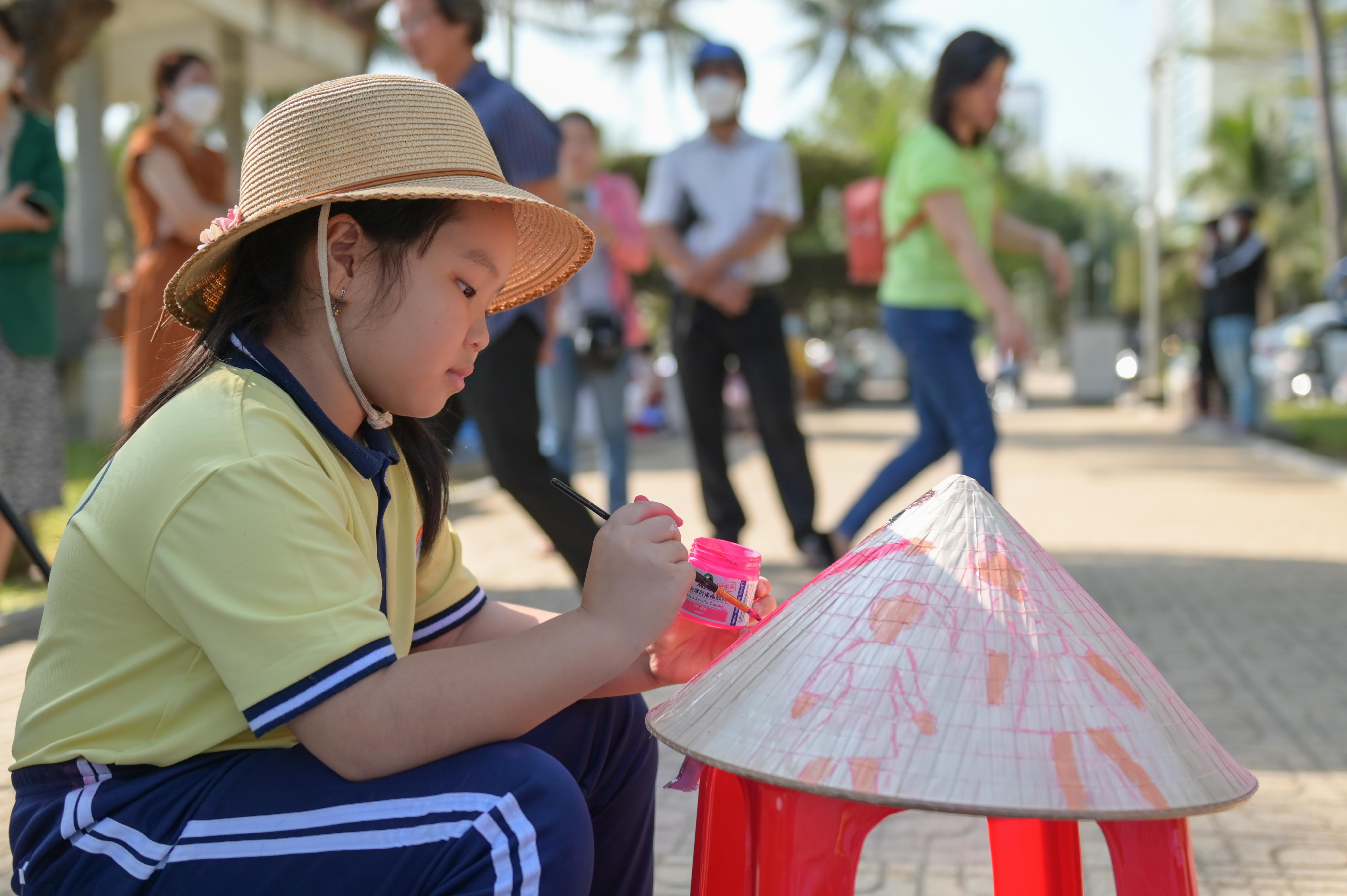 A primary school pupil painting Cham dance on a conical hat